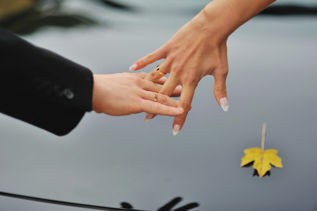 hands of a married couple with wedding rings  and yellow leaves on a background